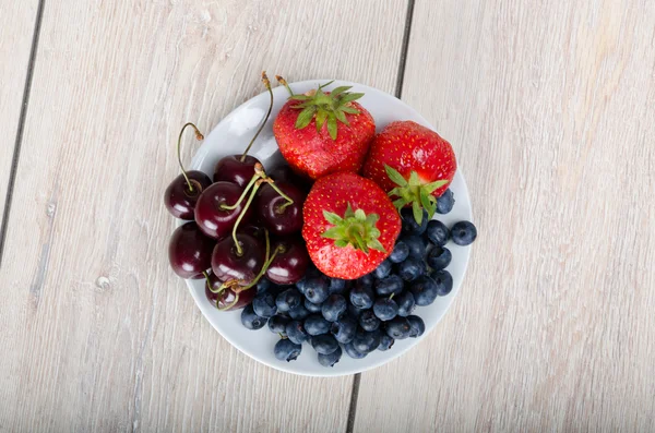 Arándanos, cerezas y fresas en un plato pequeño sobre una mesa de madera — Foto de Stock