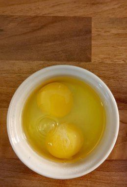 Tahta yüzey üzerinde beyaz ramekin içinde sarı sarısı olan iki çiğ yumurta.