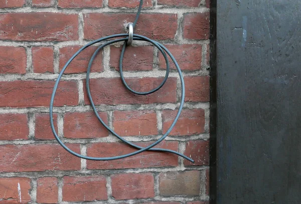 Loose electric wire hanging from loop in old brick wall. High quality photo