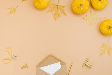 Şık bir sonbahar kompozisyon çerçevesi, balkabağı yaprakları, düşmüş akçaağaç yaprakları, kalem ve makasla kaplı bir zarf. Bej bir arkaplanda üst görünüm. Düz yat, boşluğu kopyala