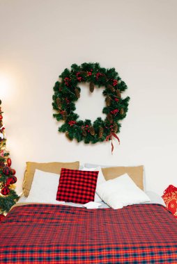 Yatak odasında kırmızı bir battaniye ve yatağın üzerinde bir Noel çelengi asılı.