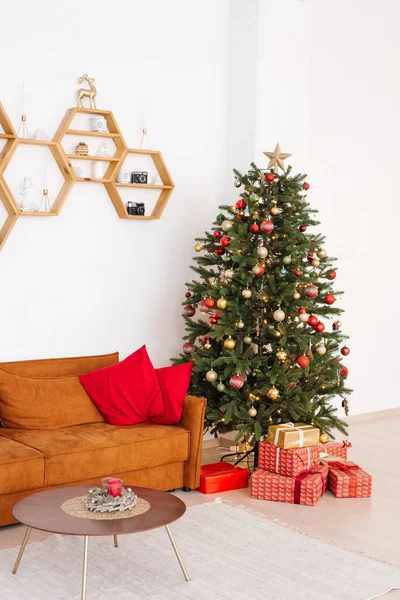 Stylish scandinavian living room with red sofa and red pillows on it, christmas tree with gifts under it