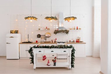 Noel 'in beyaz İskandinav mutfağının içi kırmızı dekor ve ışıklarla dolu. Mutfağın ortasında bir ada masası.