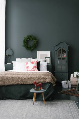 Beyaz çarşaflı yatak, karanlık bir duvara karşı, Noel çelengi ile..