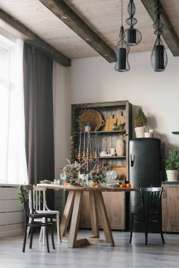 Oturma odası ya da mutfak içinde yuvarlak bir yemek masası ve Noel ve yeni yıl için dekore edilmiş bir kır evinde çeşitli sandalyeler var.