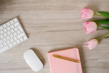 Klavye bilgisayarı, fare, pembe lale çiçekleri olan en küçük ofis masası, üzerinde kopya alanı üst görünümü olan ahşap masa.