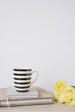 Siyah beyaz çizgili şık bir kupa iş defterlerinin üzerinde duruyor, yanında da bahar sarısı lalelerden oluşan bir buket var. Blogcu ya da serbest çalışan için tebrik kartı, Anneler Günü. Boşluğu kopyala