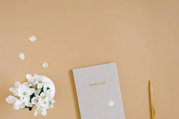 ブロガーやフリーランスの職場 ペンでベージュのノートブック ベージュのテーブルに焦点を当てて白い花 コピースペース 平置き — ストック写真