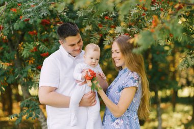 Bir yaz günü parkta Avrupalı bir aile. Anne, baba ve küçük oğul kollarında gülümsüyor.