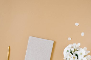 Ev konsepti dairesinden çalışma bej masanın üzerinde not defteri, kalem ve vazoyla yatıyordu. Yukarıdan bak. Boşluğu kopyala