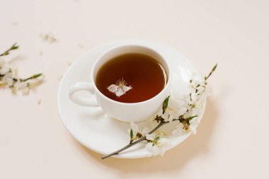 Siyah çay ve marşmelovlu beyaz porselen bardak. Çiçek açan bir elma ağacının dalları bej bir arka planda yatar.