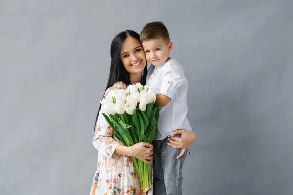 白いチューリップの花束と楽しい若い息子を持つ若い母親の肖像画 魅力的な子供 愛と幸福の概念 ロイヤリティフリーのストック写真