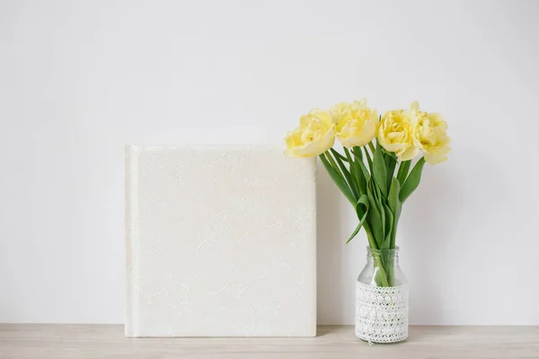 テキストのための空のスペースとテーブルの上の花瓶に黄色のチューリップの花束を持つ白い家族や結婚式の写真アルバム 家族写真アーカイブ — ストック写真