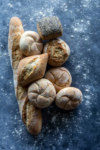 Uma variedade de pães de massa fresca e baguete contra um fundo escuro. — Fotografia de Stock
