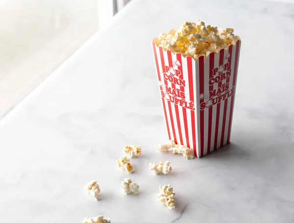 Ein hoher Karton mit frisch geknalltem Popcorn vor einem sonnigen Fenster. — Stockfoto