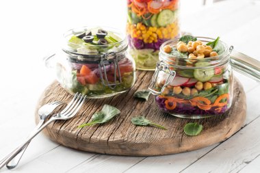 Taze salata kavanozları ahşap bir tahtanın üzerinde. Arkadan parlak bir şekilde aydınlatılmış..