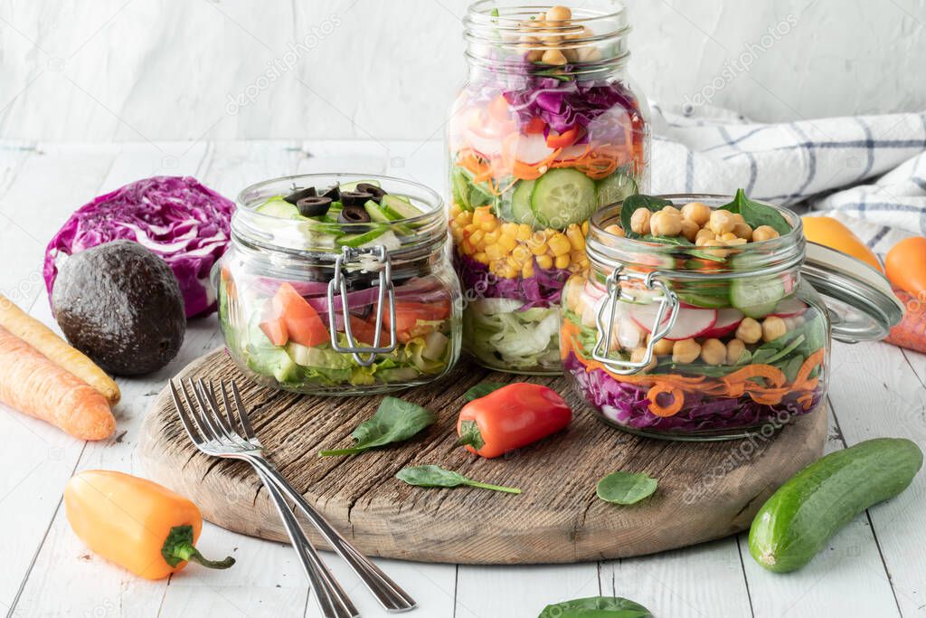 Salad jars on a rustic wooden board, with fresh ingredients all around. 