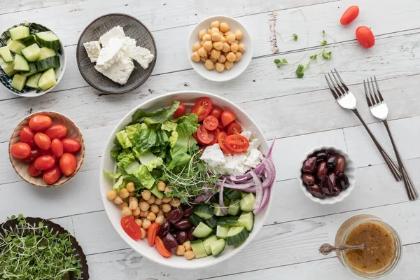 A large Greek salad bowl surrounded by smaller bowls of the ingredients. — Stockfoto