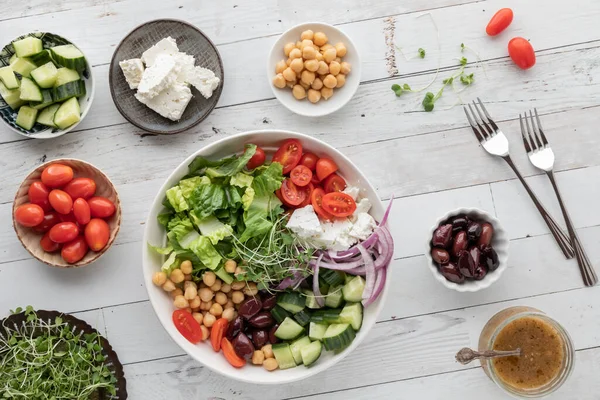 Velká řecká mísa na salát obklopená menšími miskami ingrediencí. — Stock fotografie