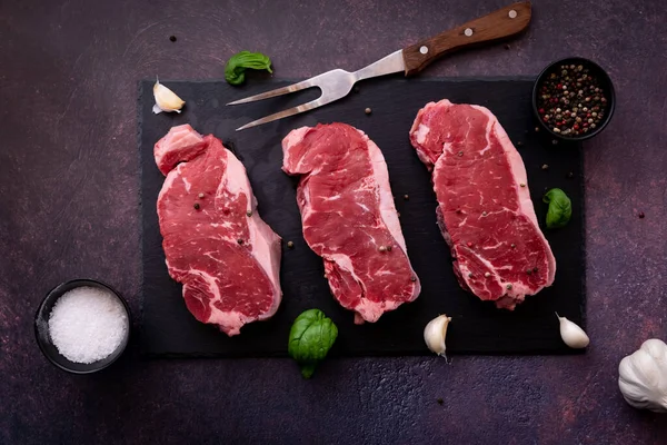 Top down view of raw striploin steaks on a black slate board, ready for grilling — Fotografia de Stock