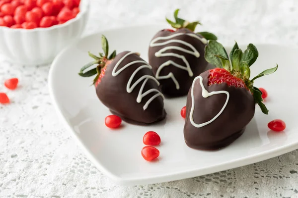 Chocolate covered strawberries on a plate with cinnamon hearts scattered around. — стоковое фото