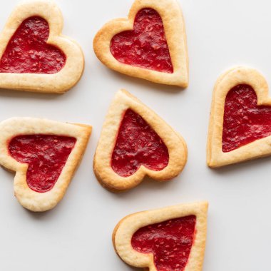 Kalp şeklindeki ahududu şeklindeki Linzer kurabiyelerinin yukarıdan görünüşü açık arkaplanlı.