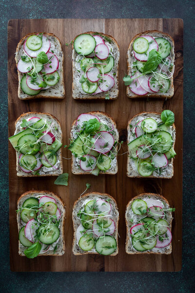 Top down view of cucumber and radish open faced sandwiches on a wooden board.