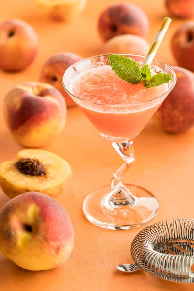 A peach Bellini cocktail garnished with mint and surrounded by peaches.
