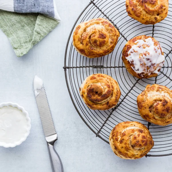 Top down view of cinnamon buns on a cooling rack served with cream cheese icing. — Stock Photo, Image