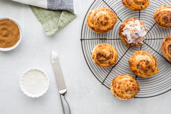 Top down view of cinnamon buns on a cooling rack served with cream cheese icing. — Stock Photo, Image