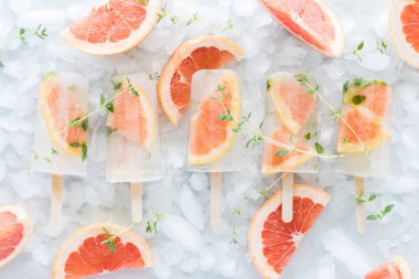 Bir sıra greyfurt ve buzdan yatağın üzerinde duran kekik şekerlerinin yukarıdan görünüşü.