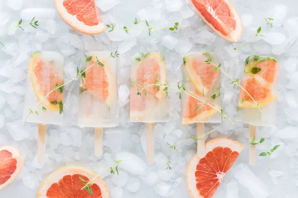 Bir sıra ferahlatıcı greyfurt kekik buzdan buzdan yatağın üzerinde, greyfurt dilimleriyle çevrili buzlu dondurma..