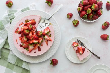 A fresh homemade strawberry cheesecake with one serving on a plate to the side, ready for eating.