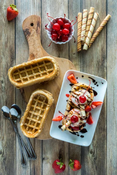 Waffle boat ice cream sundae topped with chocolate sauce, strawberries and cherries.