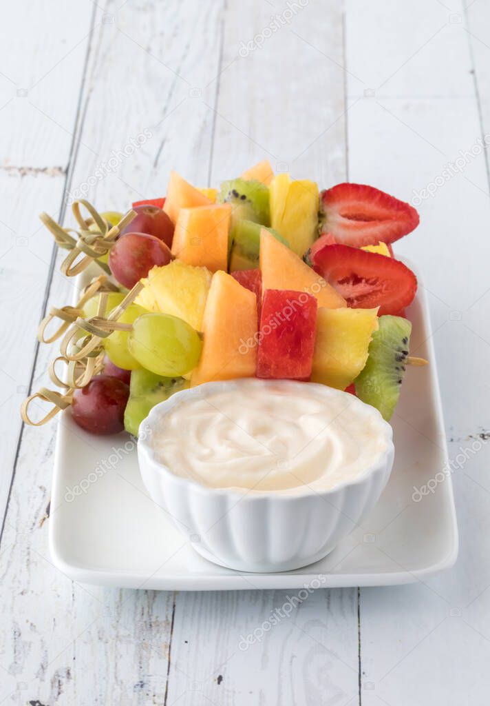 Fresh fruit kebabs on a tray served with yogurt dip, ready for eating. 