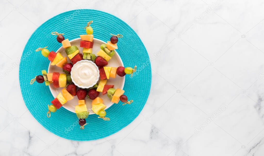 Top down view of fresh fruit kebabs on a bright blue mat with copy space to the right.