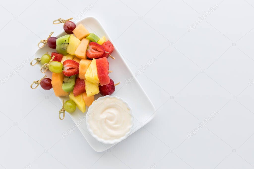 Top down view of a pile of fresh fruit skewers served with yogurt dip. Copy space to the right. 