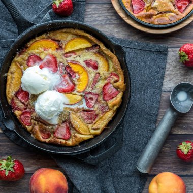 Top down view of a strawberry peach Dutch baby pancake topped with vanilla ice cream. Square crop.