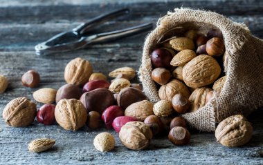 A close up of whole nuts pouring out of a burlap sack with nut crackers in behind. 