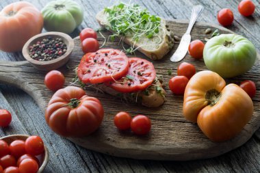 Open faced sandwiches with heirloom tomatoes and micro green sprouts, on a rustic board, ready for eating.