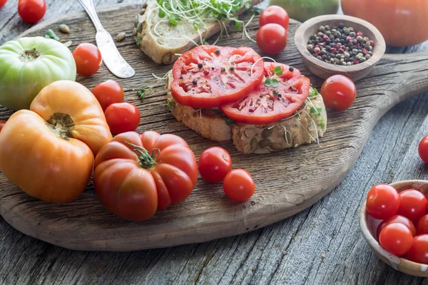 Open faced delicious heirloom tomato sandwich on a rustic board with tomatoes all around.