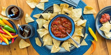 Narrow top view of a plate of crispy tortillas with salsa, served with sodas to drink. 