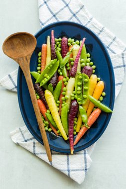 A medley of pea pods, peas and rainbow carrots on an oval plate, ready for serving.