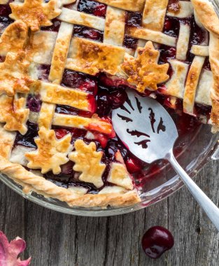 Close up view of freshly baked autumn themed lattice cherry pie with server and one slice removed. 