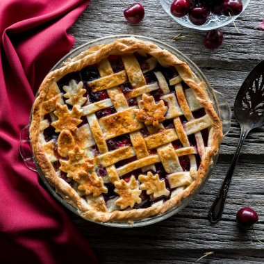 Top down view of a lattice cherry pie on a rustic wooden board, ready for serving. 