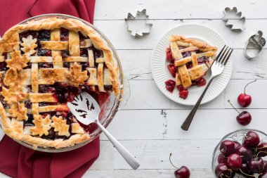 Top down view of a lattice cherry pie fresh out of the oven with one slice to the right. 