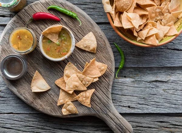 Top down view of fresh green salsa served with authentic tortilla chips, on a vintage wooden board.