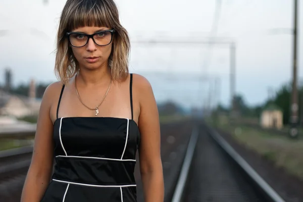 Giovane bella ragazza con gli occhiali sullo sfondo della ferrovia . — Foto Stock