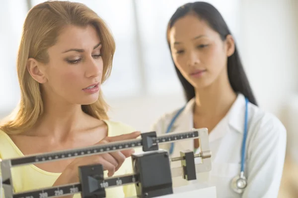 Donna che regola la scala di peso mentre in piedi dal medico femminile — Foto Stock