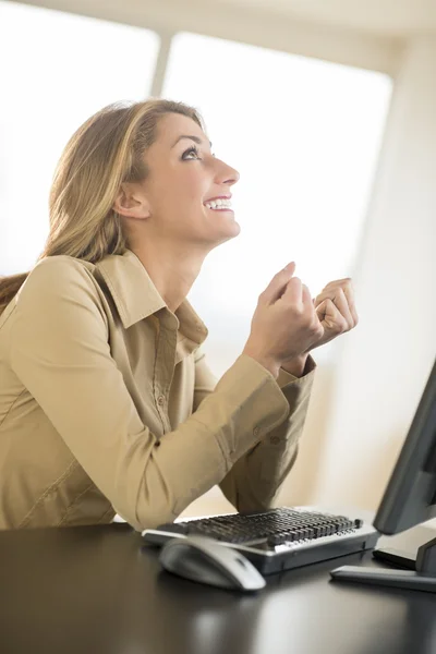 Mujer de negocios feliz mirando hacia arriba mientras está sentado en el escritorio —  Fotos de Stock